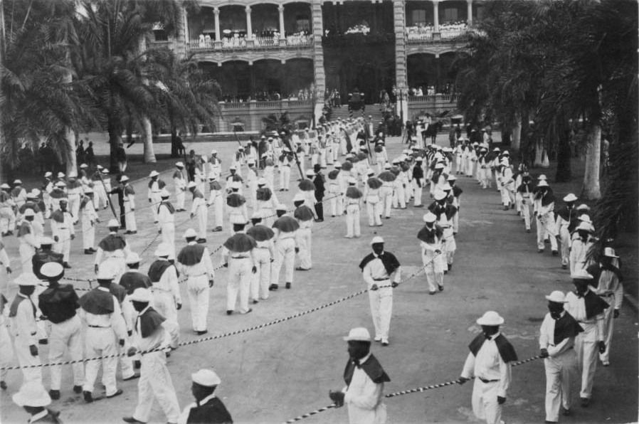 Funeral procession of Queen Liliʻuokalani with Native Hawaiian stevedores in white carrying her casket at ʻIolani Palace.